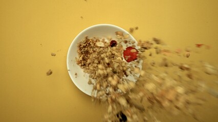 Top down view of healthy cereal falling in white bowl filled with milk with yellow background. Close up of cornflake drop in to bowl with freeze dry strawberry. Slow motion. Breakfast. Comestible.