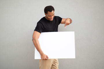 Man pointing down at blank white sign on grey background © Paula