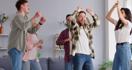 Dance party at home, happy carefree young friends dancing having fun, energetic people moving jumping in joy, amuse in modern living room interior, enjoy freedom and active youth lifestyle together