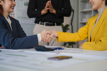 Fototapeta premium Business Deal Sealed: Two businesswomen shake hands, signifying a successful agreement, with a colleague watching in the background. This image embodies trust, partnership.