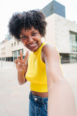 Vertical. Young African American woman taking a selfie while showing a peace sign in a urban...