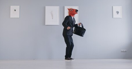 Happy business man or corporate employee in an animal mask having fun at the end of work day. Funny man wearing a suit and disguised in a horse mask holding his briefcase and dancing in the office