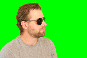 Surprised wow man over green background. Adult bearded guy in sunglasses gesturing on green screen chromakey. Handsome male looking pointed side to product placement isolated greenscreen. For Keying