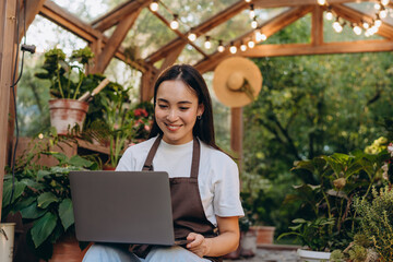 Portrait of cheerful florist in dark overall over simple outfit sending emails to potential clients of garden station