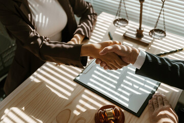 Lawyers shaking hands after signing a contract in a law office, with a gavel and legal scales in...