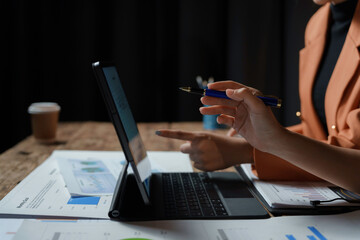 Two businesswomen working together, analyzing financial charts and data on a digital tablet, pointing at the screen with a pen
