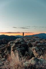 A lo lejos una joven mujer fot&oacute;grafa admirando un paisaje de monta&ntilde;as al amanecer