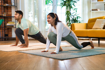 Indian Asian couple happily doing One-Legged Wide-Legged Forward Bend pose at home together