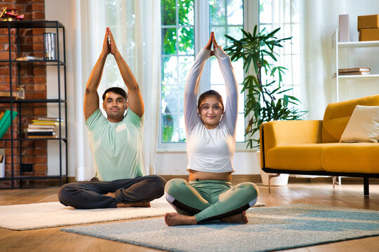 Indian Asian couple performing Parvatasana, seated mountain yoga pose at home in a lavish room - Powered by Adobe