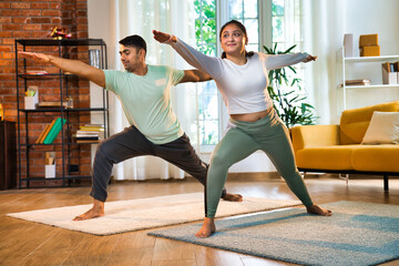 Indian couple happily practicing standing Virabhadrasana pose at home, embodying strength