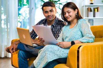Indian Asian couple happily budgeting and working on finances with laptop and documents at home