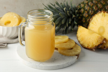Tasty pineapple juice in mason jar and fresh fruits on white wooden table against grey background, closeup