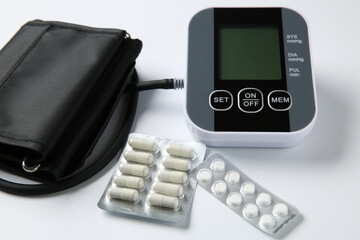 Blood pressure measuring device and pills on white background, closeup