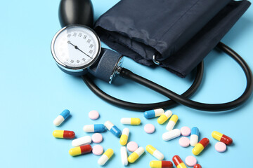 Blood pressure measuring device and pills on light blue background, closeup