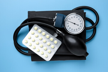Blood pressure measuring device and pills on light blue background, top view