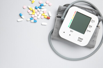 Blood pressure measuring device and pills on light grey background, top view. Space for text
