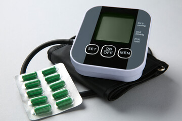 Blood pressure measuring device and pills on light grey background, closeup