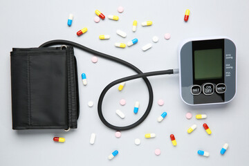 Blood pressure measuring device and pills on light grey background, top view