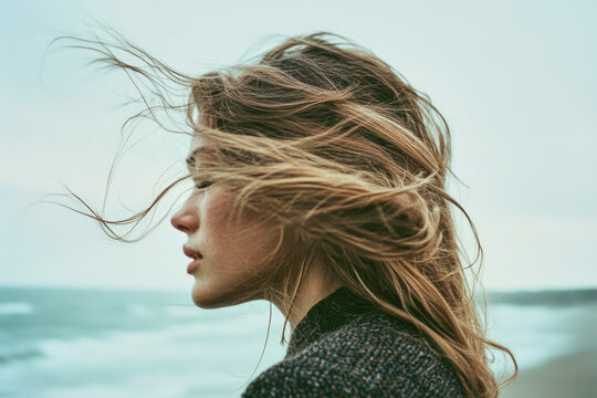 A woman enjoys a windy day on the coast with her hair flowing freely, embracing the natural beauty around her