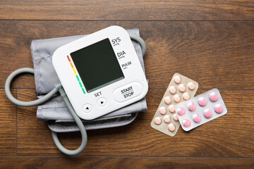 Blood pressure measuring device and pills on wooden table, top view