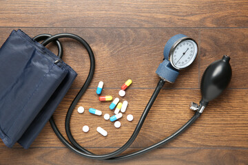 Blood pressure measuring device and pills on wooden table, top view