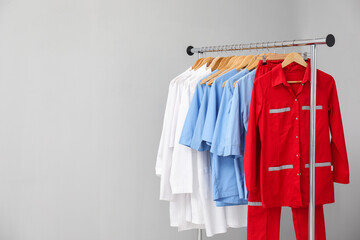 Different medical workers' uniforms on clothing rack against grey background. Space for text