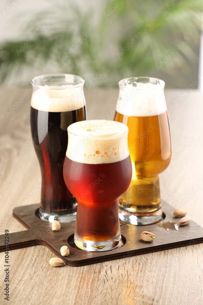 Poster Glasses with different types of beer and pistachio nuts on wooden table indoors