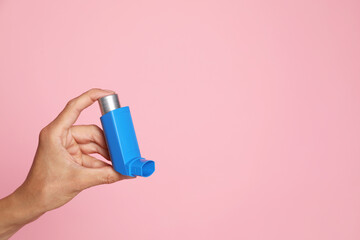 Woman holding asthma inhaler on pink background, closeup. Space for text