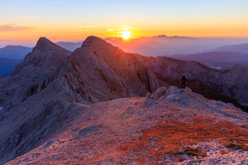 hiking girl stands on a mountain during sunrise against the sun and enjoys the warm morning sun...