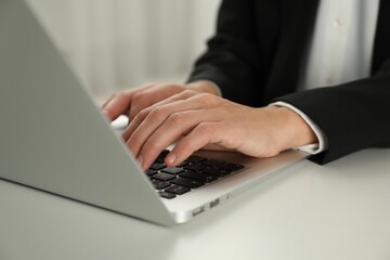 Businesswoman using laptop at white table indoors, closeup. Modern technology