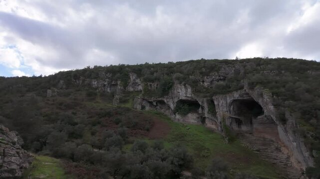 Buracas do Casmilo at Condeixa - Portugal. Ancient limestone caves nestled in a rugged hillside, featuring multiple natural cavern openings amid green vegetation and moss-covered rock formations on a 