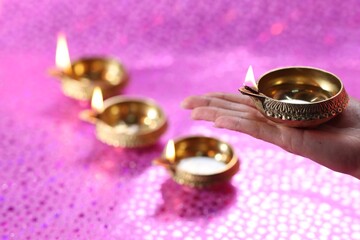 Diwali celebration. Woman holding lit diya lamp on pink background, closeup