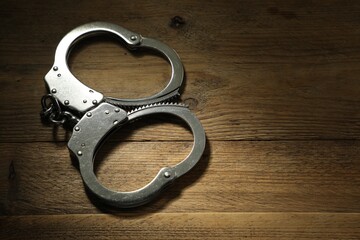 Classic chain handcuffs on wooden table, closeup. Space for text