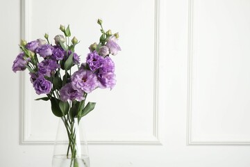 Vase with beautiful eustoma flowers near white wall, space for text