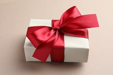 Gift box with red bow on beige background, closeup