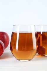 Fresh apple juice in glasses and fruits on white wooden table
