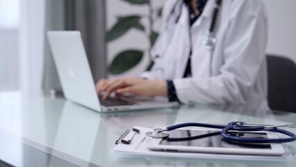 Tablet computer and blue stethoscope are on the glass table while doctor woman is using laptop computer on the glass table. Medicine concept