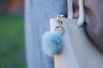 Woman with faux fur keychain on her bag outdoors, closeup. Selective focus