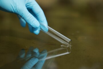 Examination of water quality. Researcher taking water sample from lake outdoors, closeup