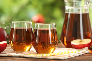 Tasty freshly made apple juice in glasses on wooden table outdoors
