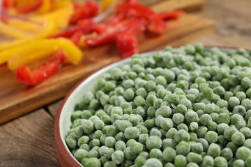 Frozen green peas in bowl on wooden table, closeup