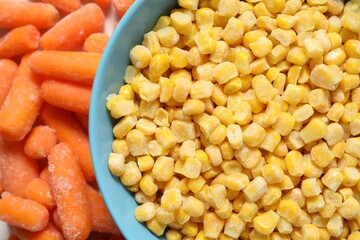 Frozen corn kernels in bowl and baby carrots on table, top view