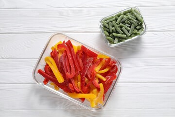 Frozen green beans and bell peppers in glass containers on white wooden table, top view