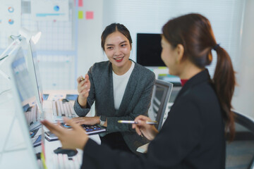 Two smiling businesswomen having a discussion about work, reviewing paperwork and data on computer screen