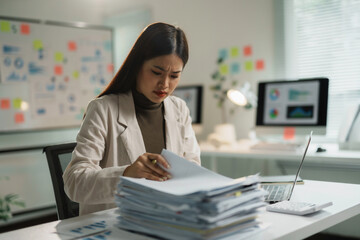 Businesswoman feeling stressed and tired while working with a lot of documents on the table at...