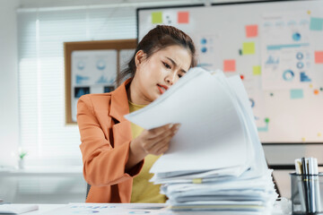 Businesswoman is looking frustrated while searching through a stack of documents at her desk in the office