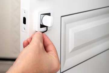 A locksmith repairs the door latch of a white modern door with a hexagonal tool. Close-up.