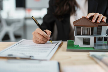 Real estate agent signing contract while keeping hand on house model in a real estate agency
