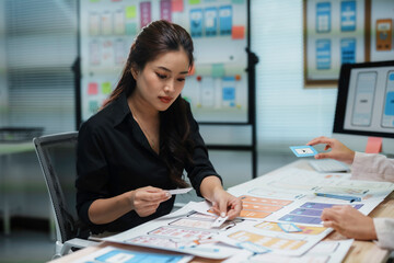 Asian uiux designers working together on mobile app design in their office, choosing the perfect icons for their project