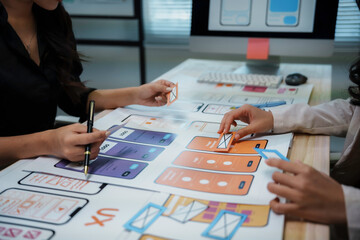 Two ux designers are discussing user experience of mobile application prototype on a table with...